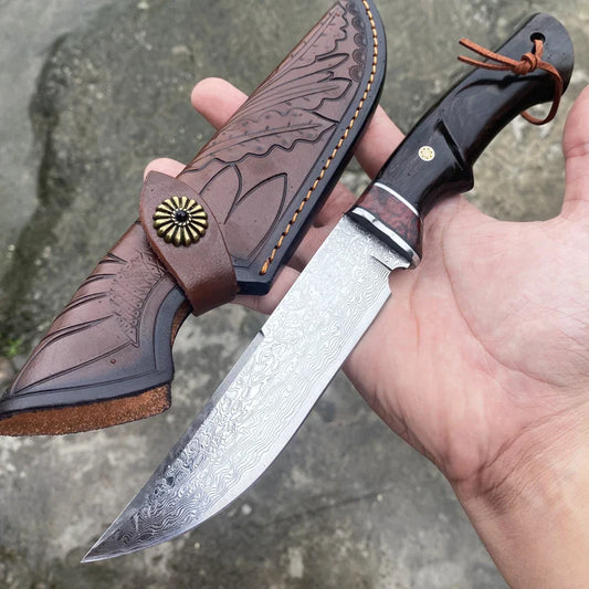 VG10 Damascus hunting knife with patterned blade and dark wooden handle held alongside engraved leather sheath